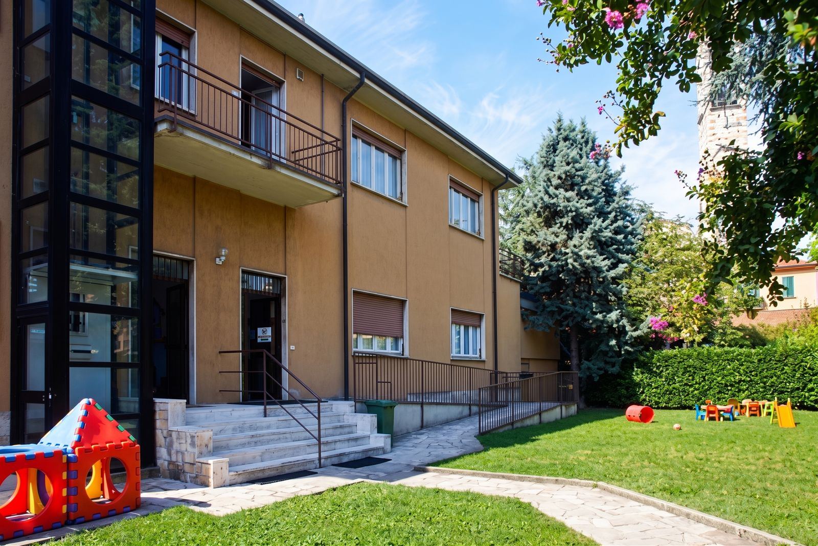 La facciata del nido con l'ingresso, la rampa e il giardino con giochi e tavolini colorati