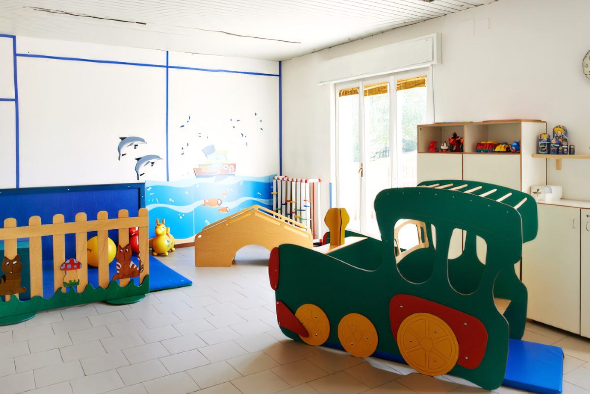 La sala giochi con il trenino di legno, lo spazio morbido e il mare dipinto sulla parete